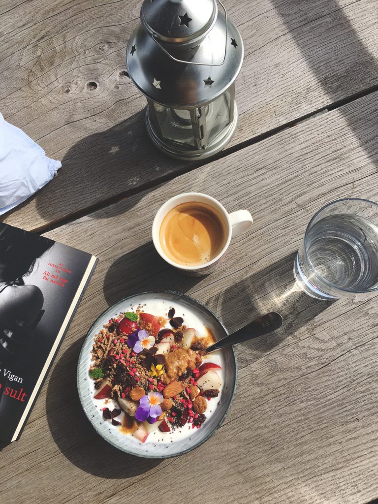 morgenmad på altanen, kaffe, yoghurt med granola og frugt, bog